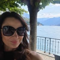 Woman wearing sunglasses by a lakeside railing with mountains and water in the background
