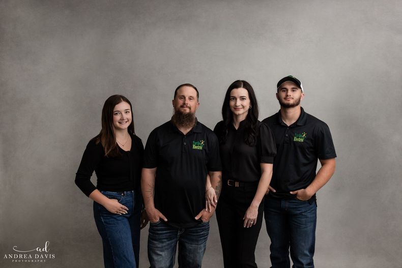 Four adults standing together in black shirts against a gray studio backdrop