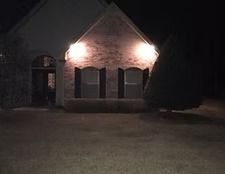 Night view of a brick house with three lit windows and a dark lawn in front