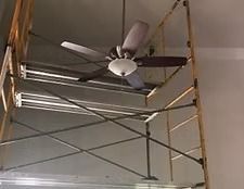 Ceiling fan mounted on metal scaffolding in an unfinished indoor space