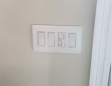 White wall light switch panel with four switches beside a doorframe