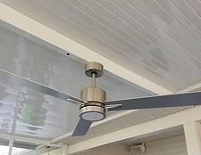 Close-up of a brushed metal ceiling fan on a light-colored covered porch ceiling