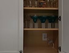 Open cabinet with shelves, teal glasses, and an electrical outlet in the back.