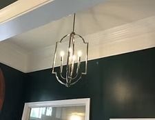 Modern chandelier hanging from a white ceiling in a dark green room above a doorway