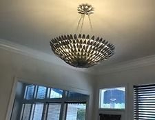 Modern chandelier hanging from a ceiling in a bright room with windows and blinds