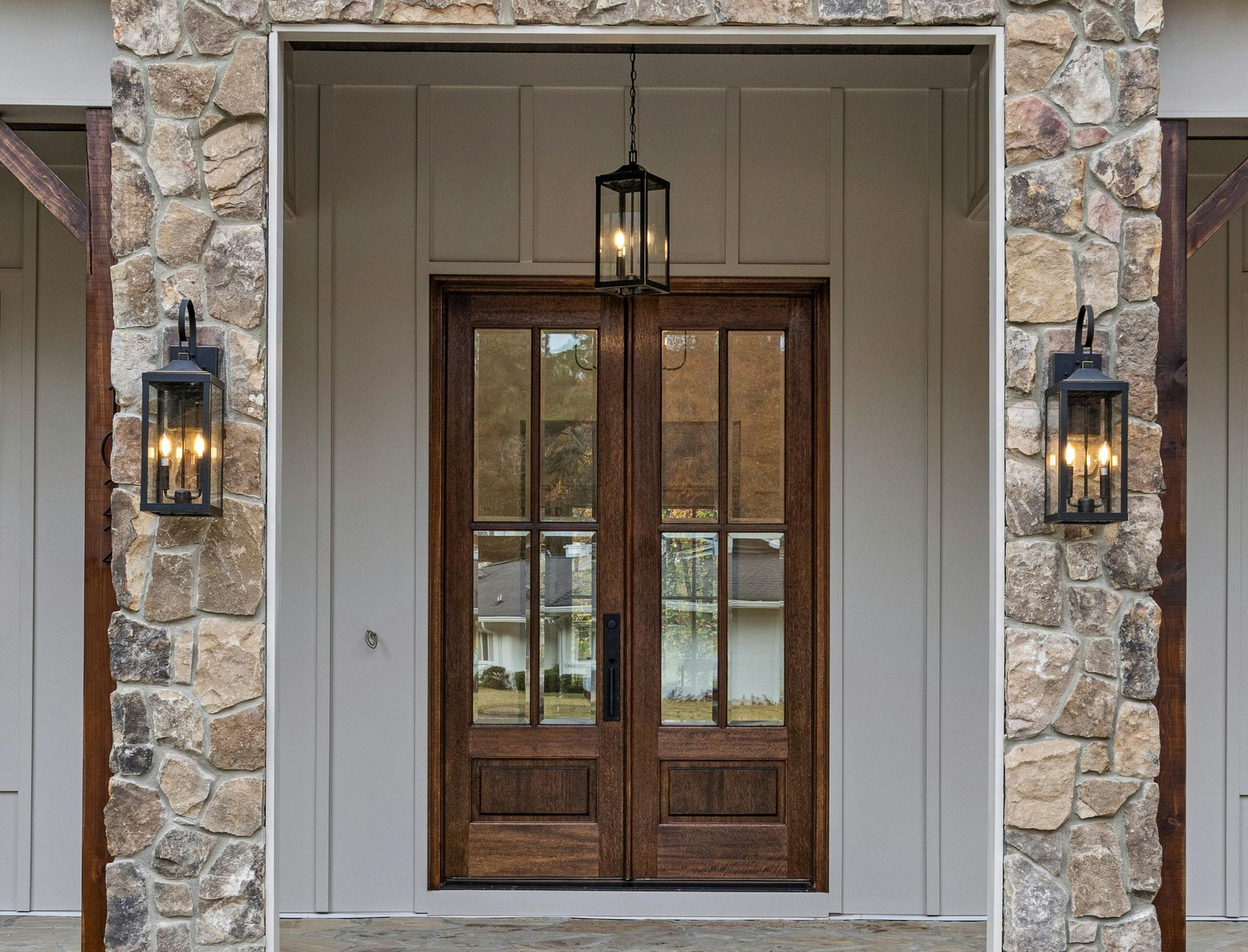 Stone-framed front entry with double wooden doors and black lanterns
