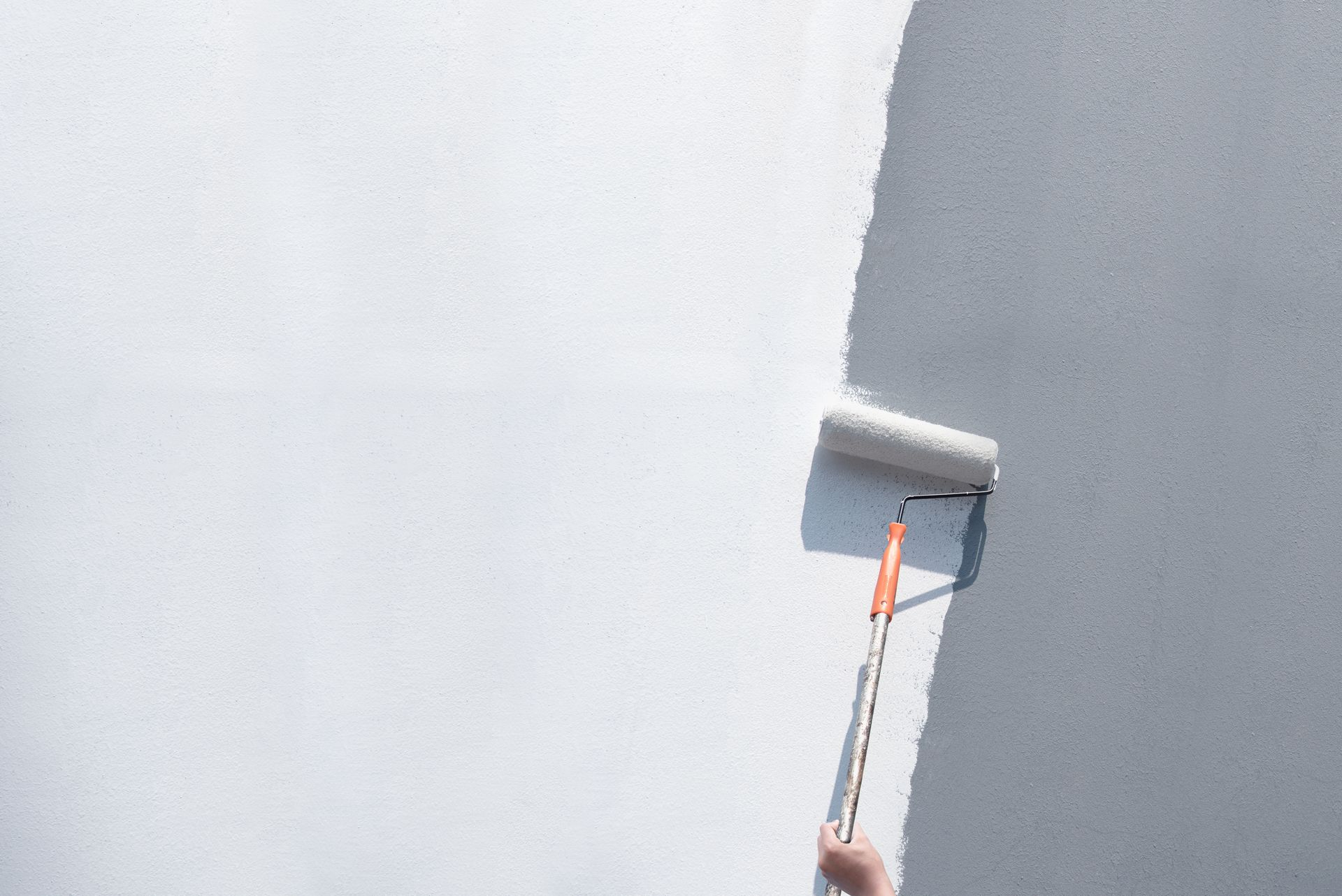 Une personne peint un mur blanc avec un rouleau à long manche