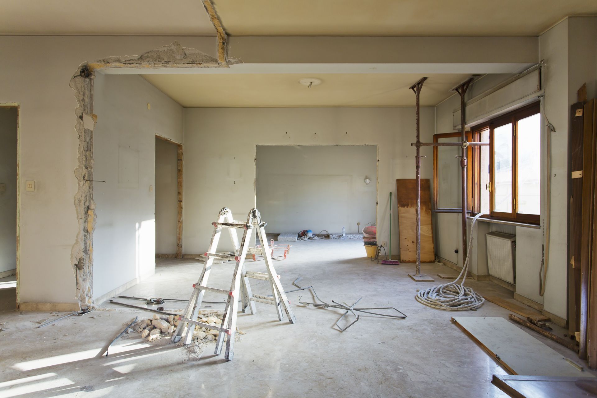 Pièce partiellement rénovée avec échelles, débris de construction et murs et fenêtres apparents