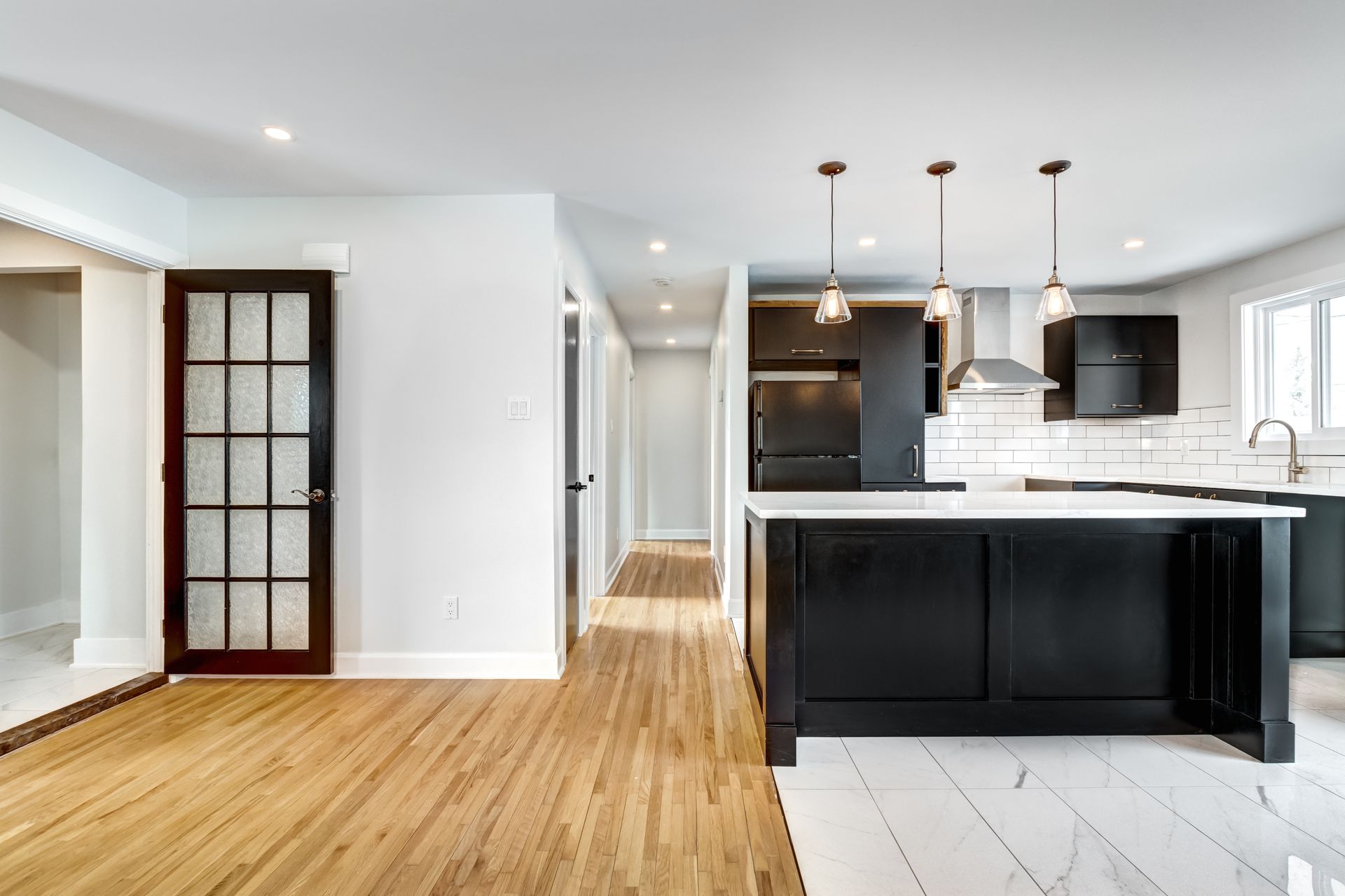 Cuisine et salle à manger modernes avec îlot noir, armoires blanches, parquet et grandes fenêtres