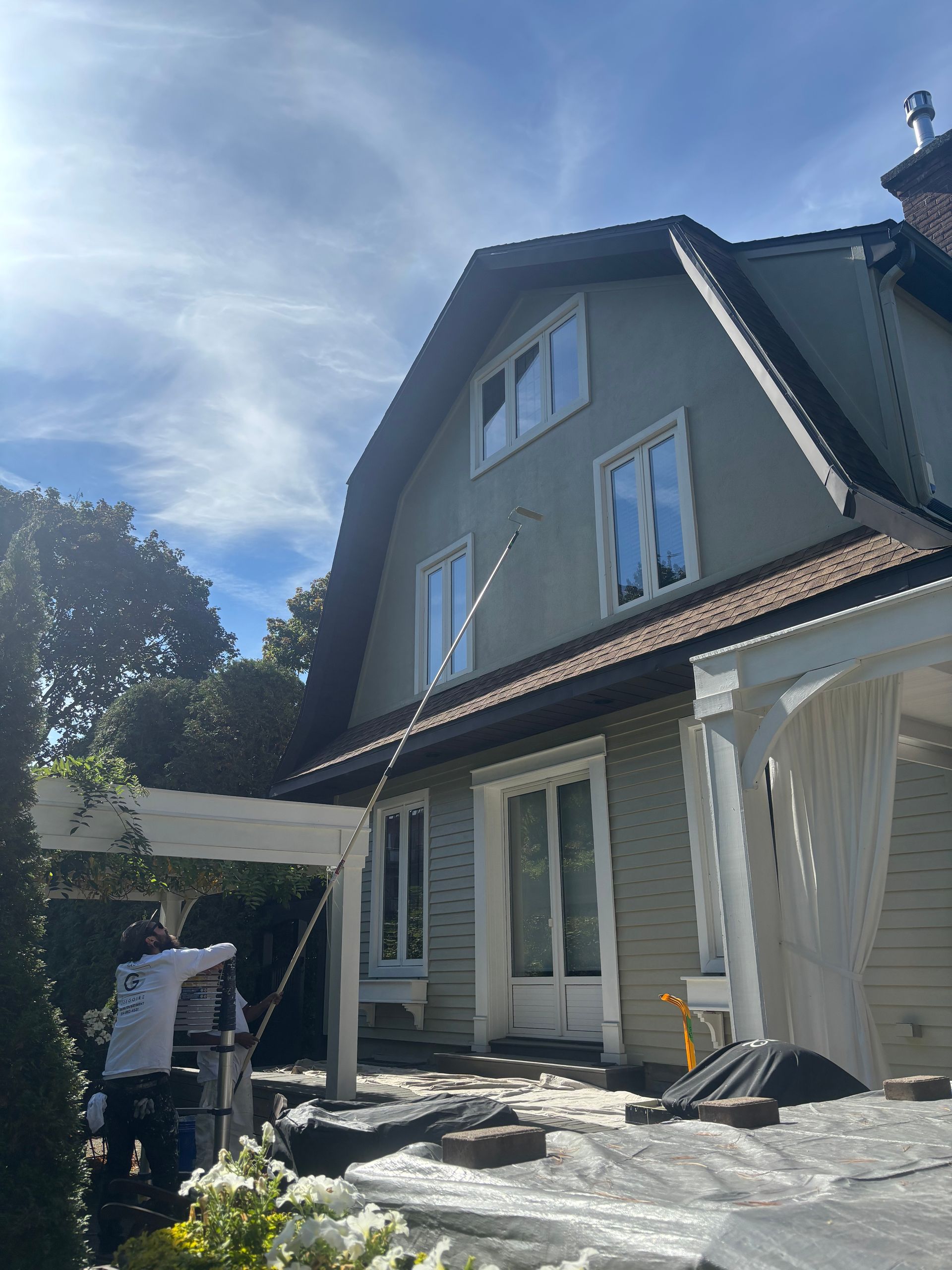 Extérieur d'une maison avec des ouvriers utilisant des bâches en plastique et du matériel dans une cour ensoleillée