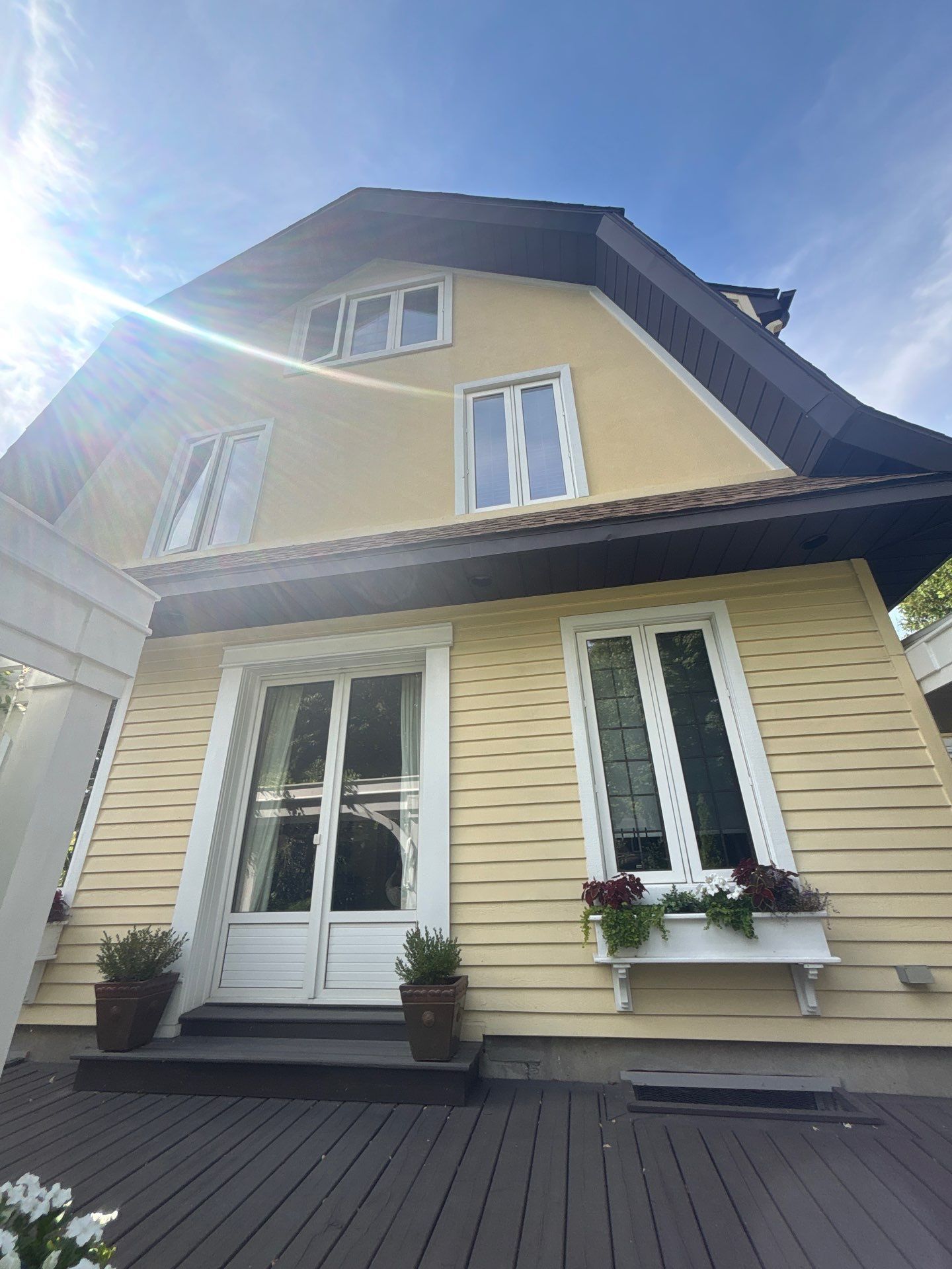 Maison jaune avec fenêtres à encadrement blanc et toit sombre, vue en contre-plongée.
