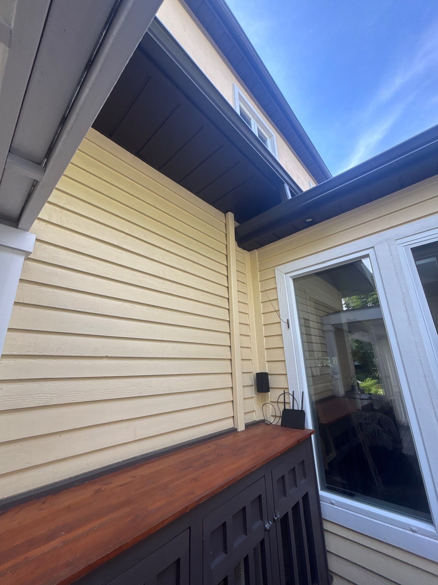 Allée extérieure couverte avec bardage beige, rambarde en bois et porte coulissante en verre sous un ciel bleu