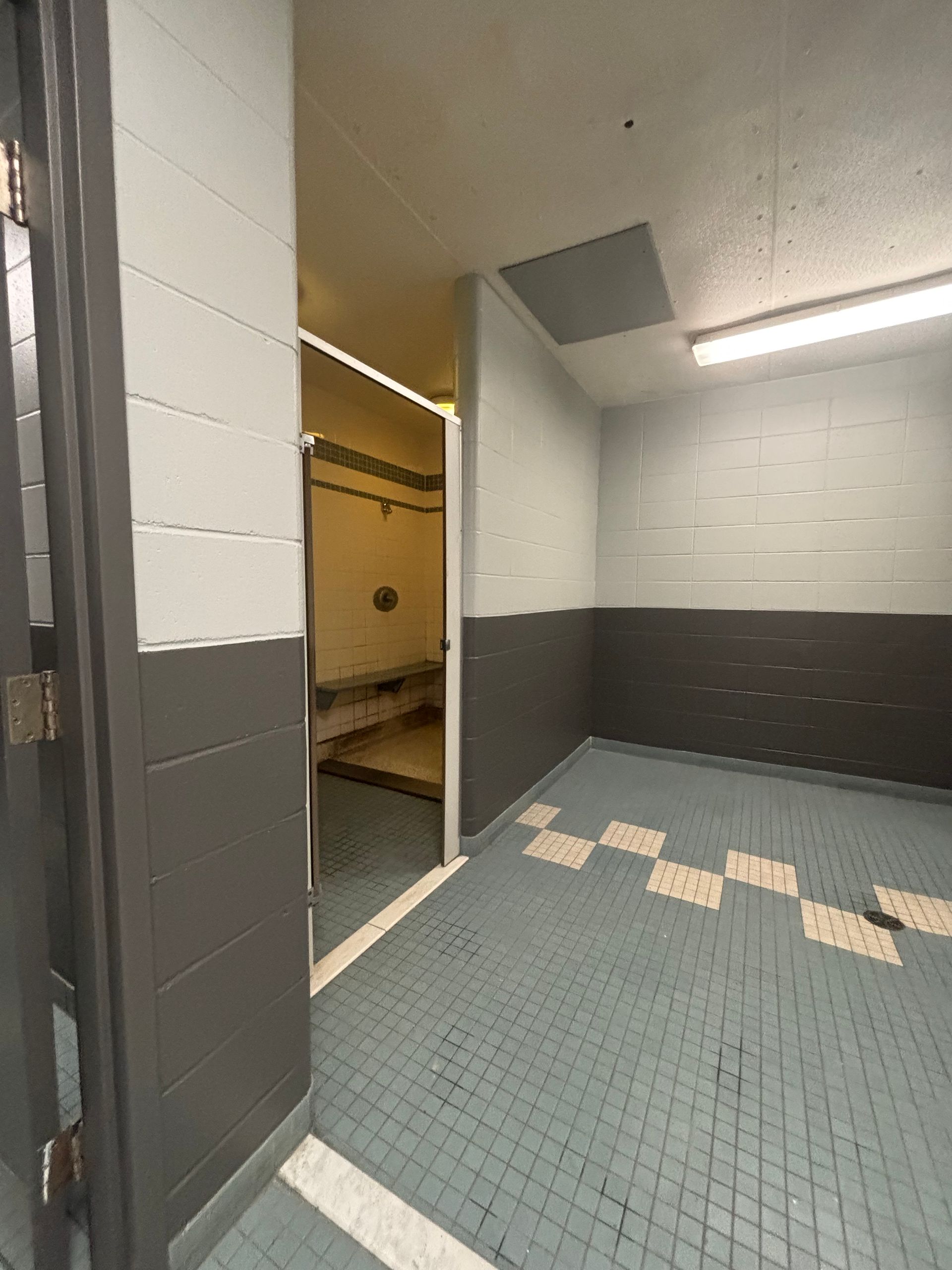 Couloir carrelé vide avec une porte ouverte et un plafonnier fluorescent, laissant apparaître des murs blancs et gris.