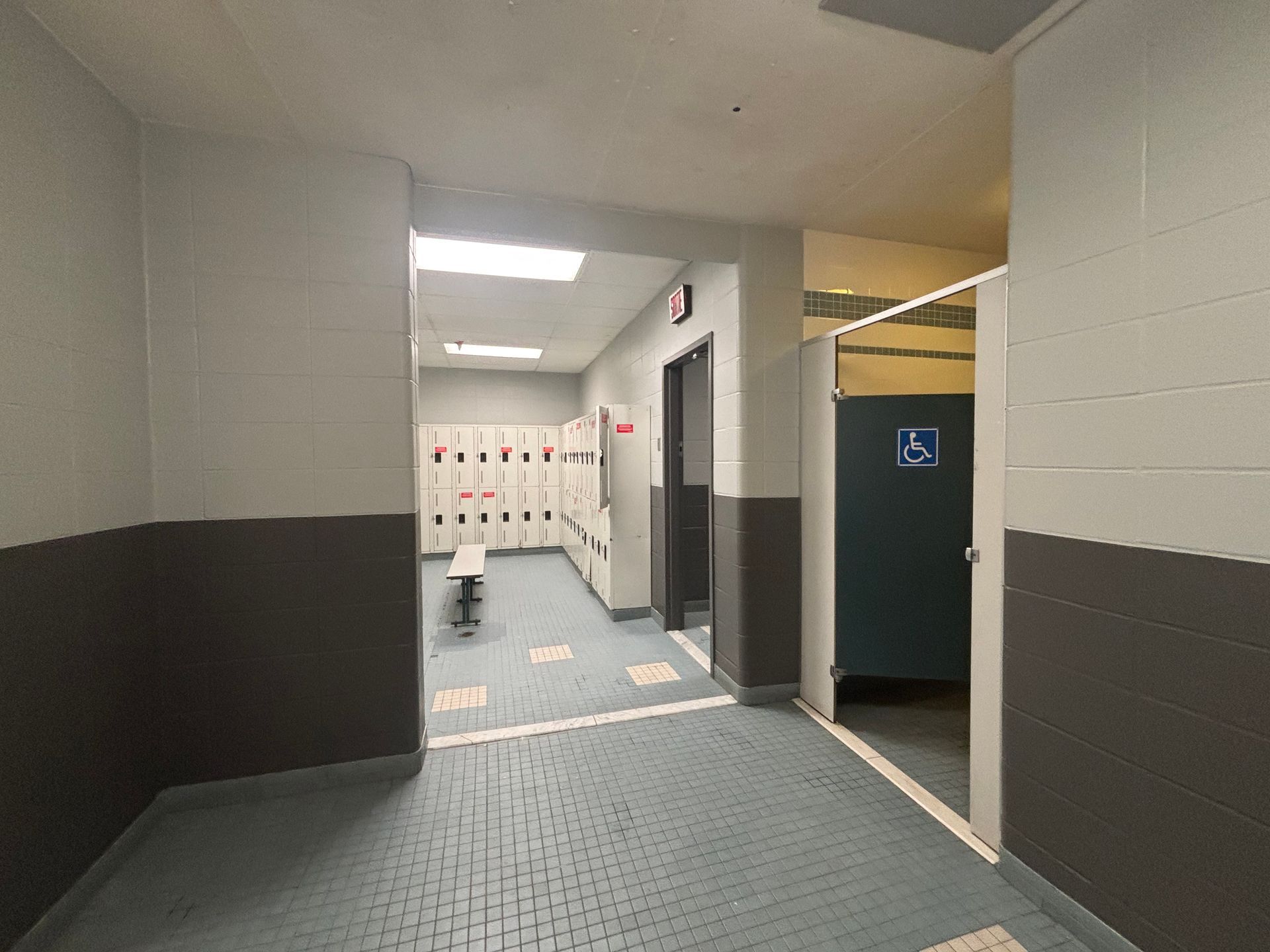 Couloir intérieur avec moquette bleue, casiers et porte ouverte donnant sur les toilettes
