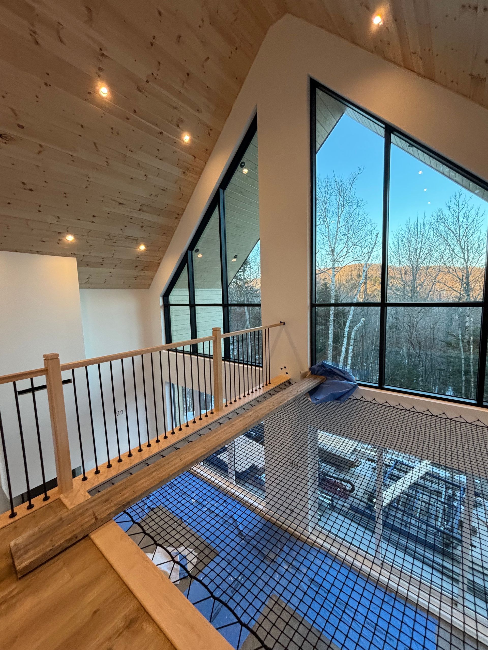 Intérieur de loft moderne avec plafond en bois, grandes fenêtres et mezzanine vitrée donnant sur les arbres