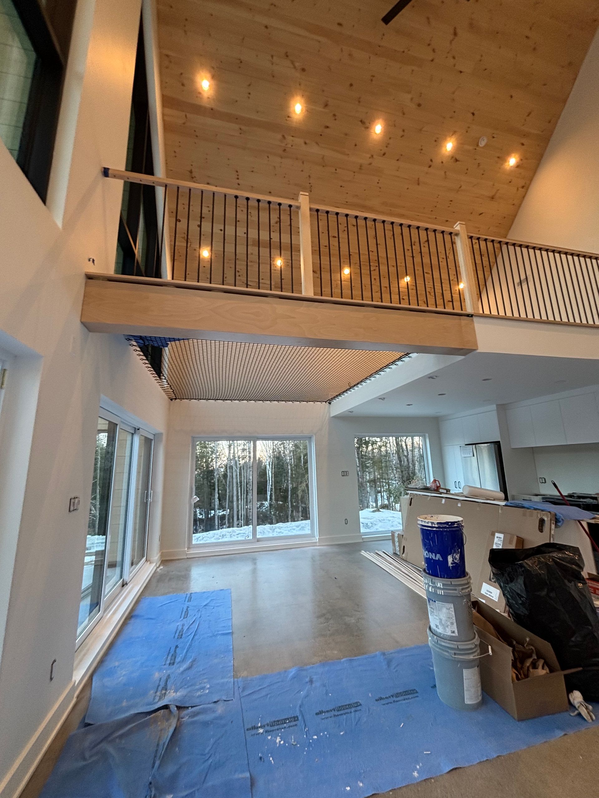 Salon moderne ouvert avec mezzanine, plafond en bois, grandes fenêtres et matériaux de construction au sol