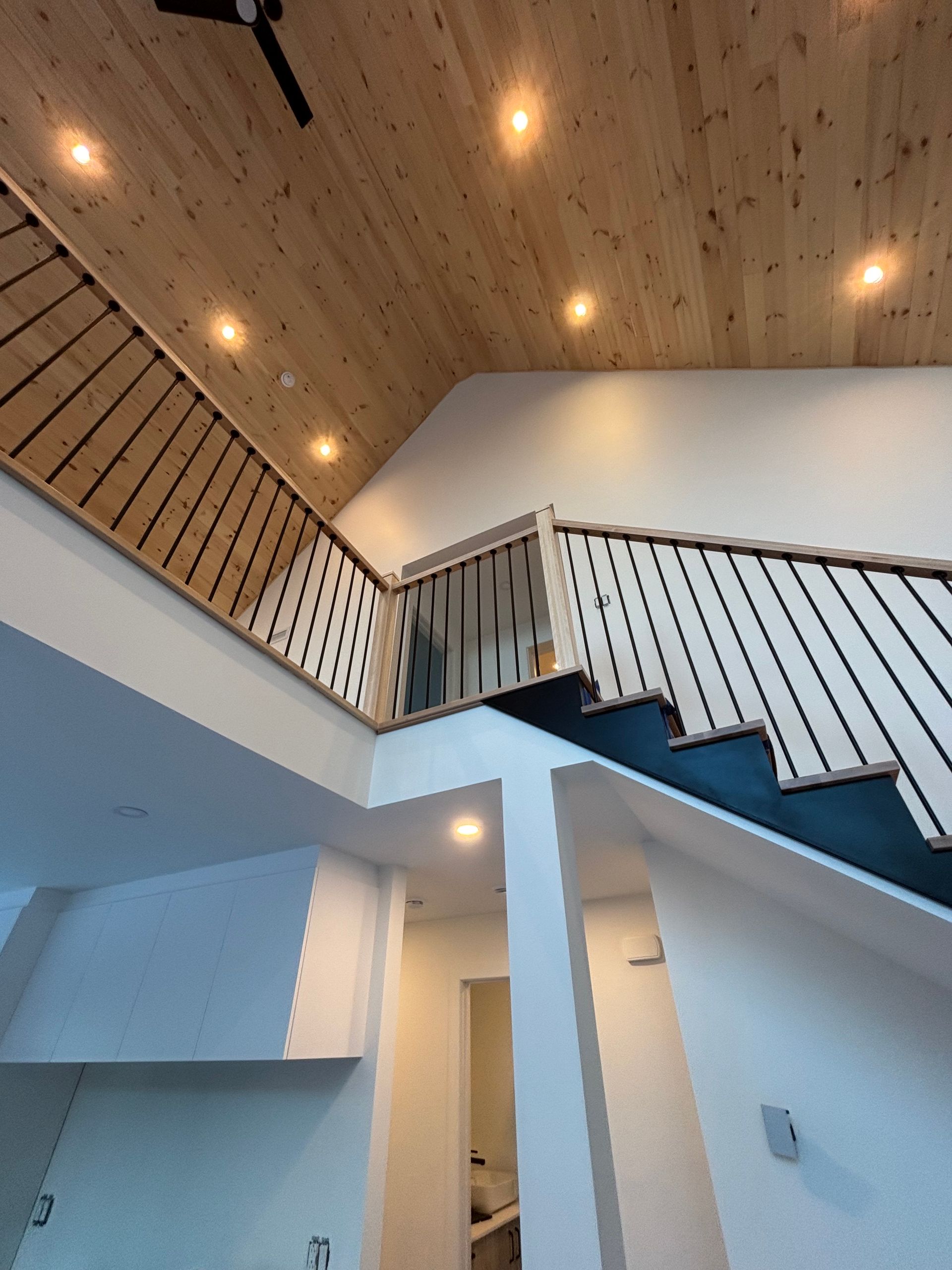Escalier intérieur moderne avec rampe foncée, plafond en bois et éclairage encastré dans un hall d'entrée lumineux