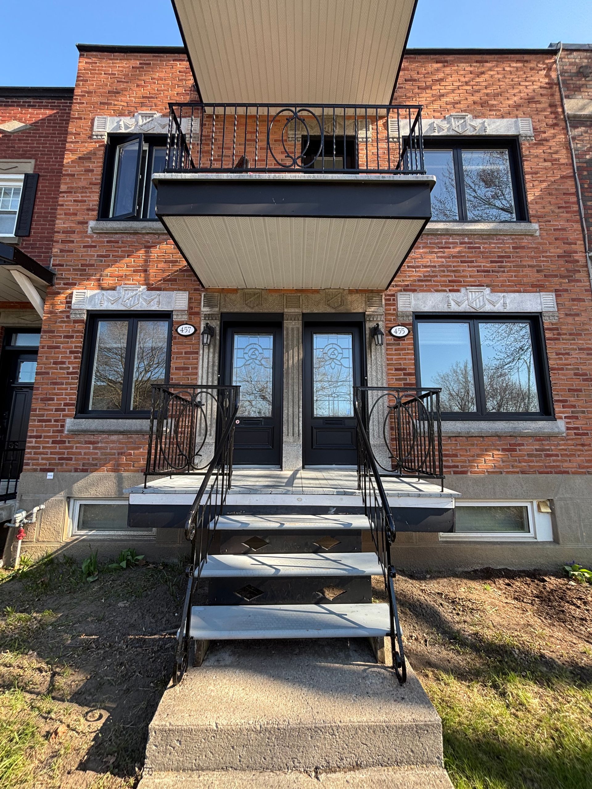 Immeuble d'appartements en briques avec escalier d'entrée, balcons et portes noires
