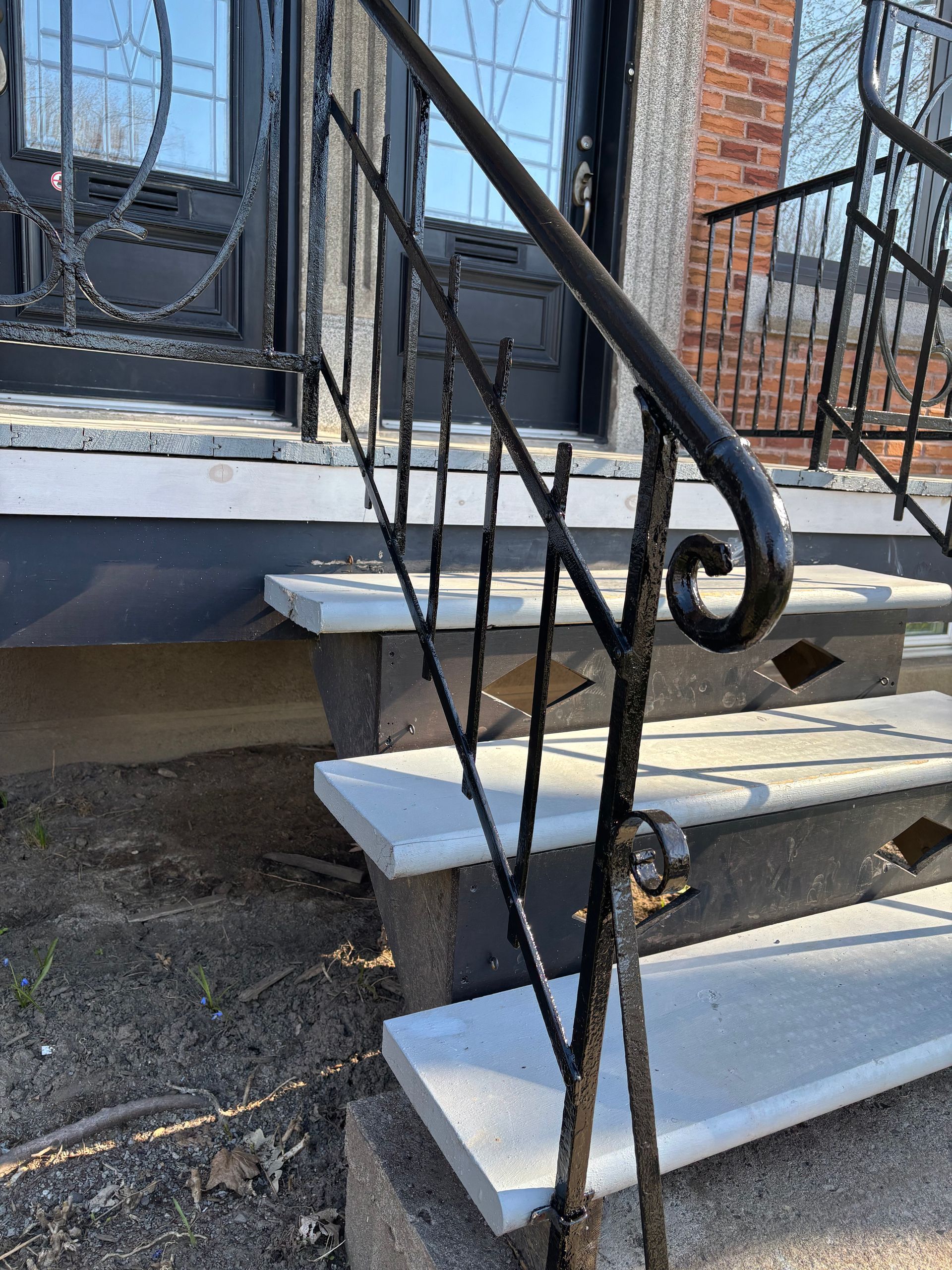 Marches d'entrée d'une maison avec escalier peint en blanc, rampe en fer noir et façade en briques.