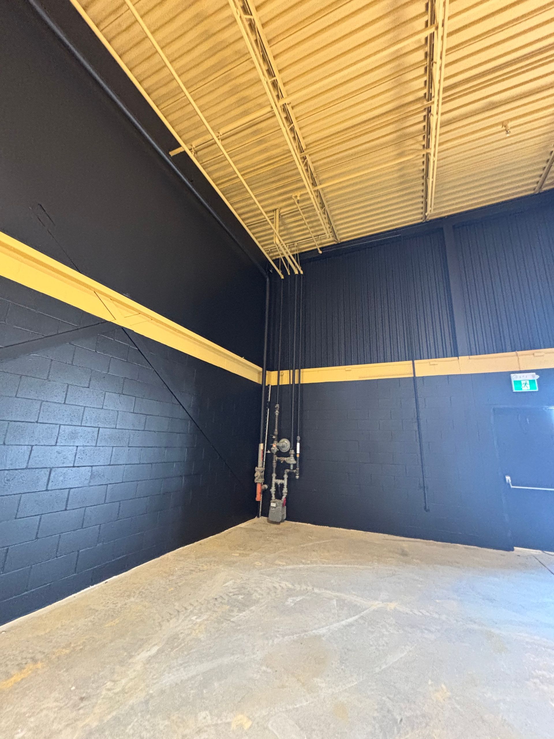 Coin d'entrepôt vide, murs noirs, bande jaune et sol en béton sous un haut plafond ouvert