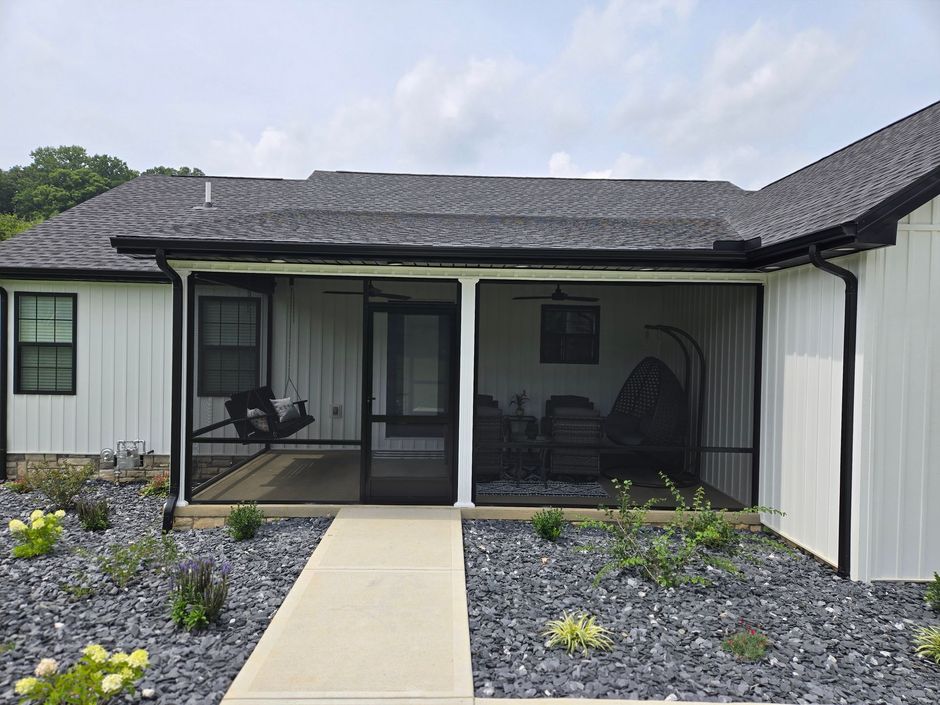 A modern white house with a black-framed screened-in porch, a concrete walkway, and gray stone landscaping.