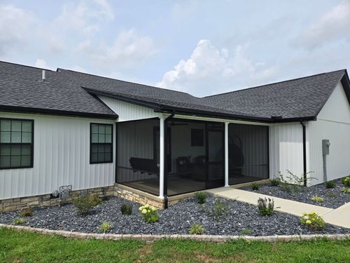 A white house with black trim and a dark gray shingled roof, featuring a screened-in back porch and gravel landscaping.