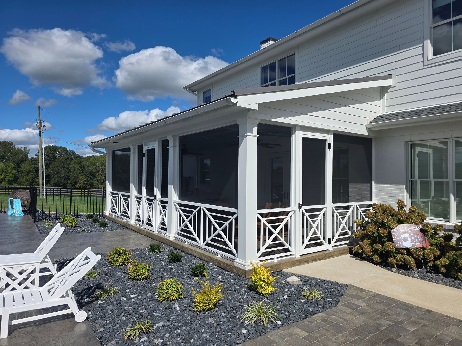 A white house with a screened-in porch, patio furniture, and landscaping on a sunny day.