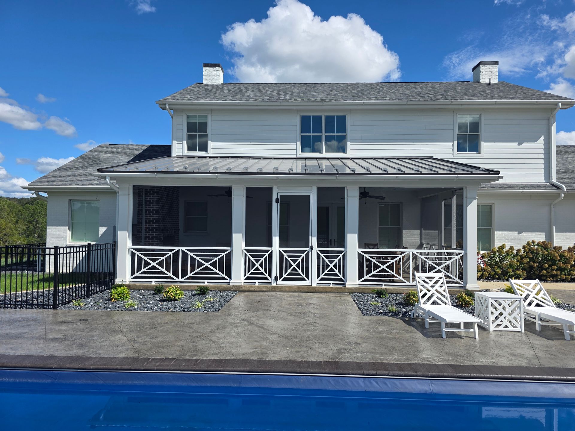 A white two-story house with a screened-in porch and pool deck, featuring white lounge chairs and a blue pool.