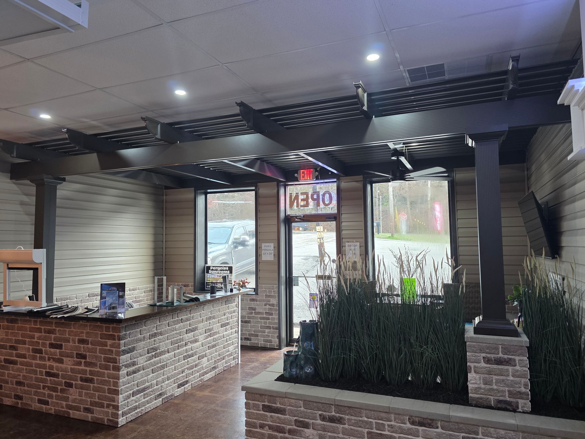 A retail reception area with a brick counter, a wooden pergola ceiling feature, and indoor plants near the entrance.