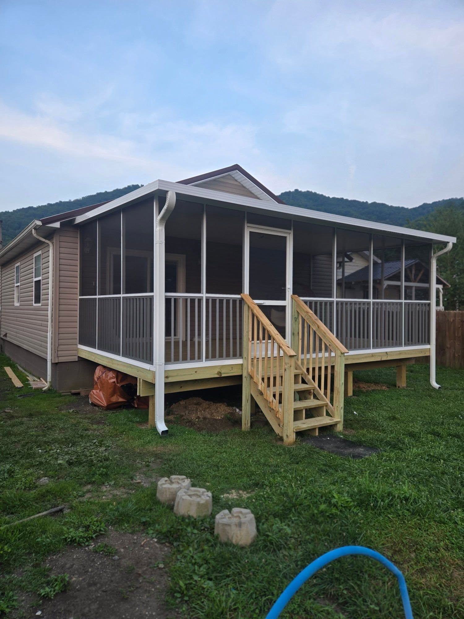 A light-colored house with a newly constructed, wood-framed screened-in porch and stairs, set against mountain hills.