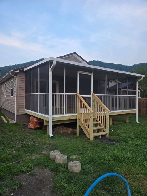 A light-colored house with a newly constructed, wood-framed screened-in porch and stairs, set against mountain hills.