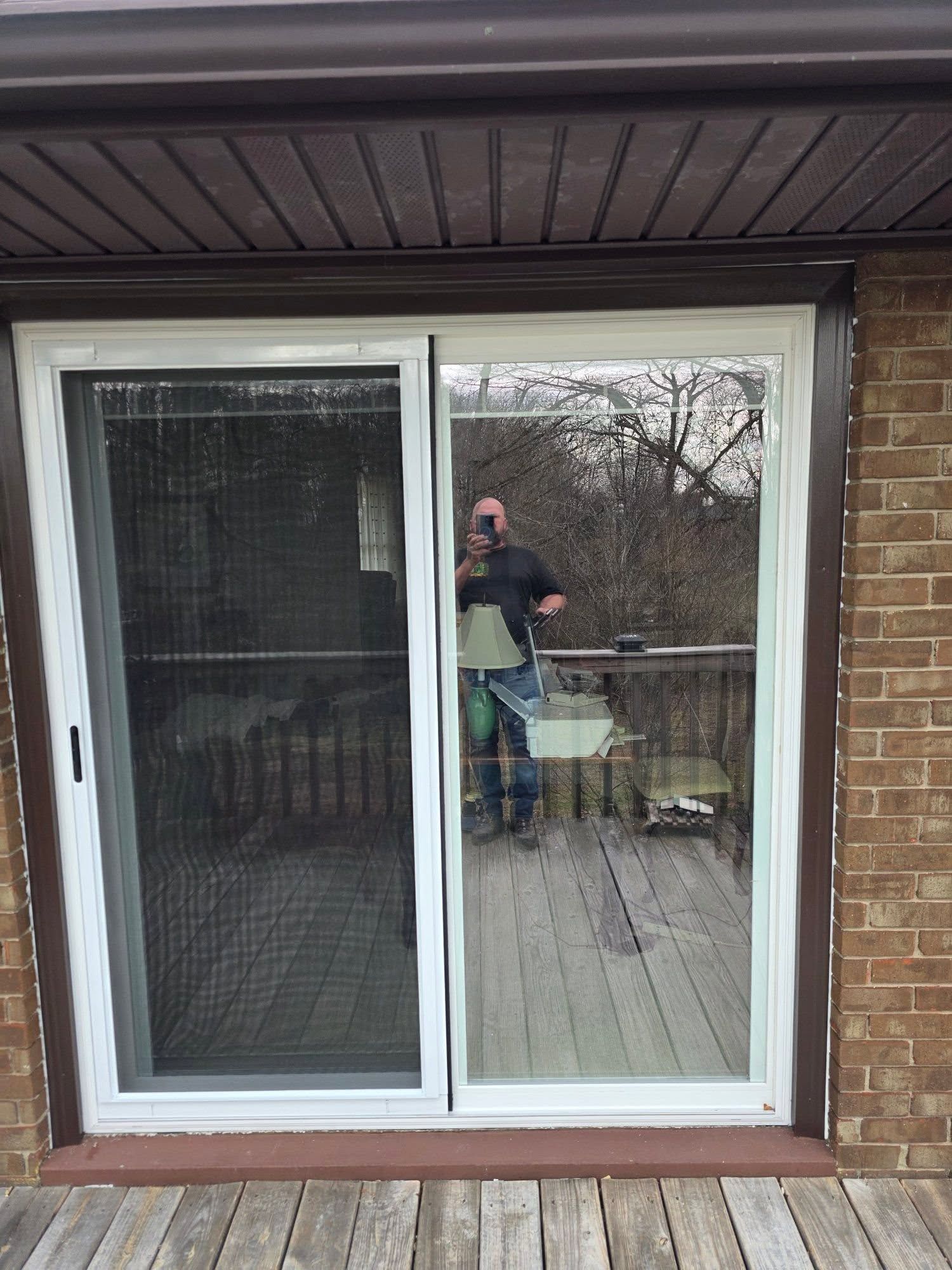 A white sliding glass door with a screen, reflecting a person taking the photo on an outdoor wooden deck.