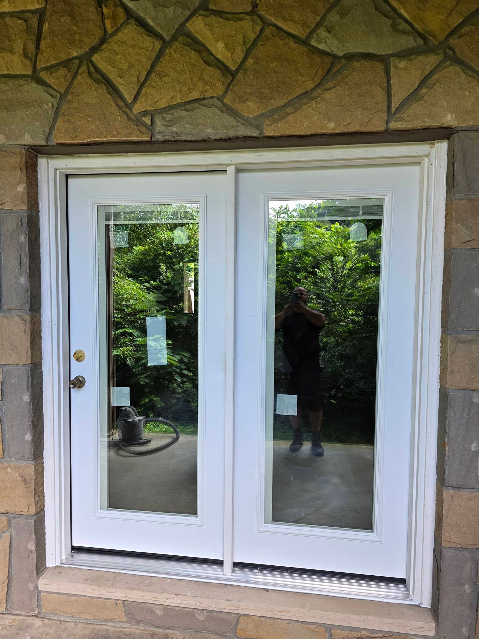 White double doors with glass panes set in a stone wall. A person is visible in the reflection of the glass.