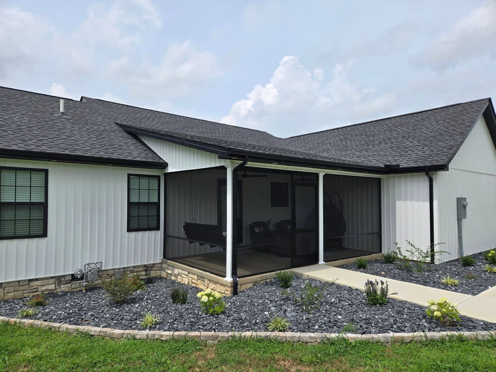 A modern white farmhouse with dark trim and roof, featuring a screened-in back porch and landscaped stone garden.
