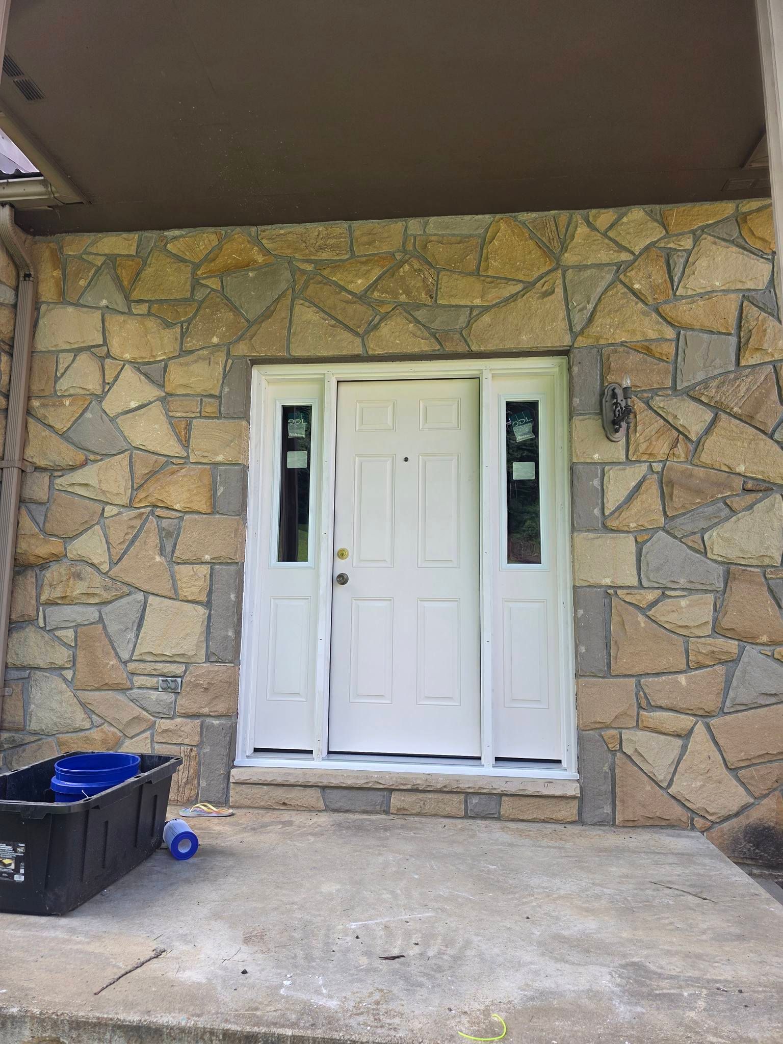 White front door with sidelights centered on a tan and gray stone wall porch.