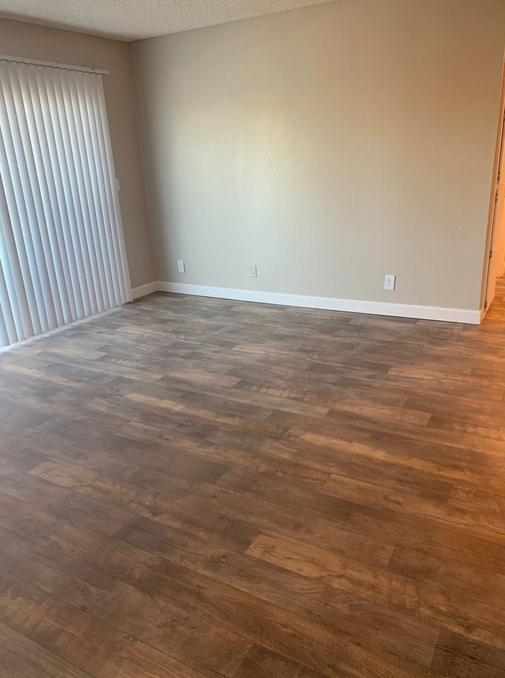 Empty room with wood-look flooring, beige walls, and sliding glass door blinds.