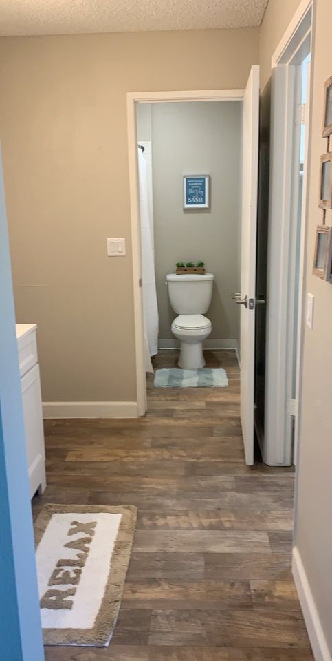 Hallway with wood-look flooring leading to a bathroom with a toilet and framed wall art.