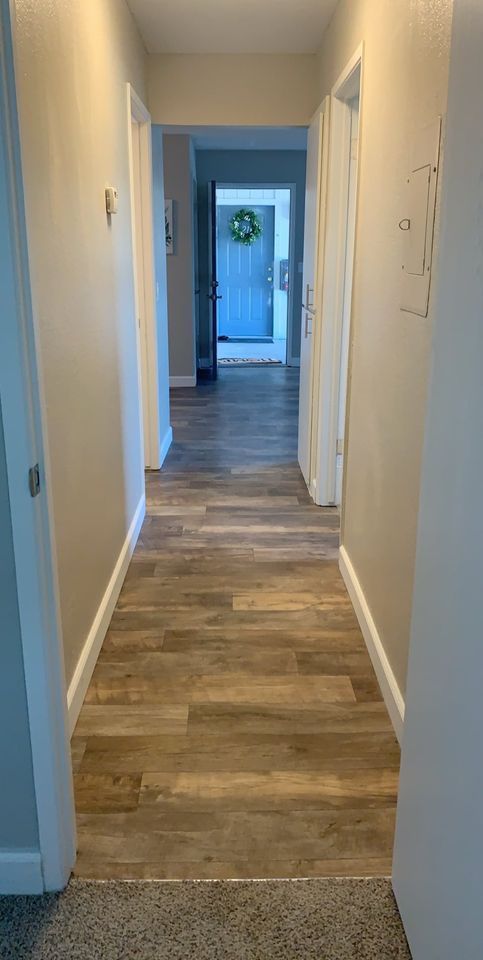 Narrow hallway with wood-look flooring and white walls, leading to a blue door at the end.