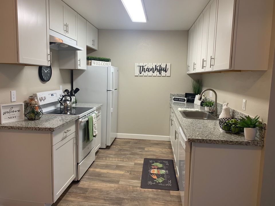 Small kitchen with white cabinets, beige walls, and a stove, sink, fridge, and countertop decor.