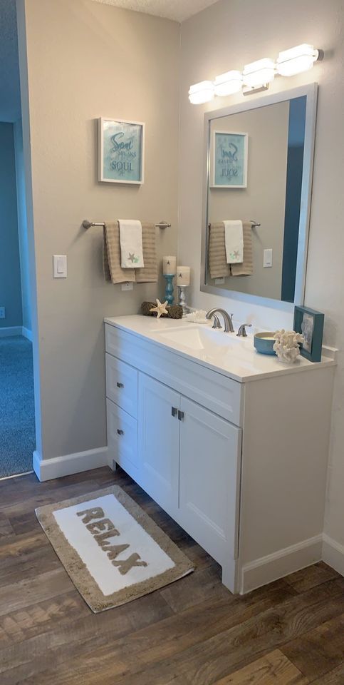 Bright bathroom vanity with mirror, lights, sink, and navy-and-white decor on a wood floor.