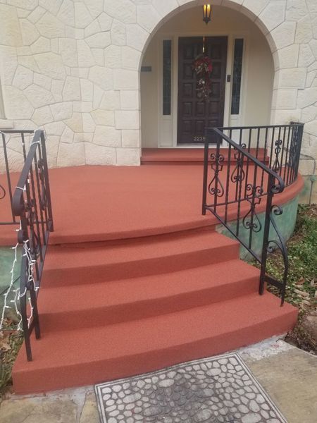 A front porch with red steps and a wrought iron railing.