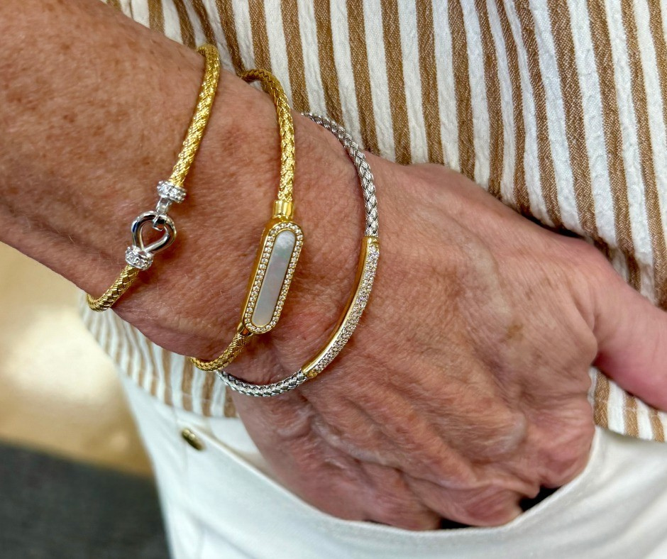 Three gold and silver bracelets on a person's wrist, hand in a pocket; striped shirt.