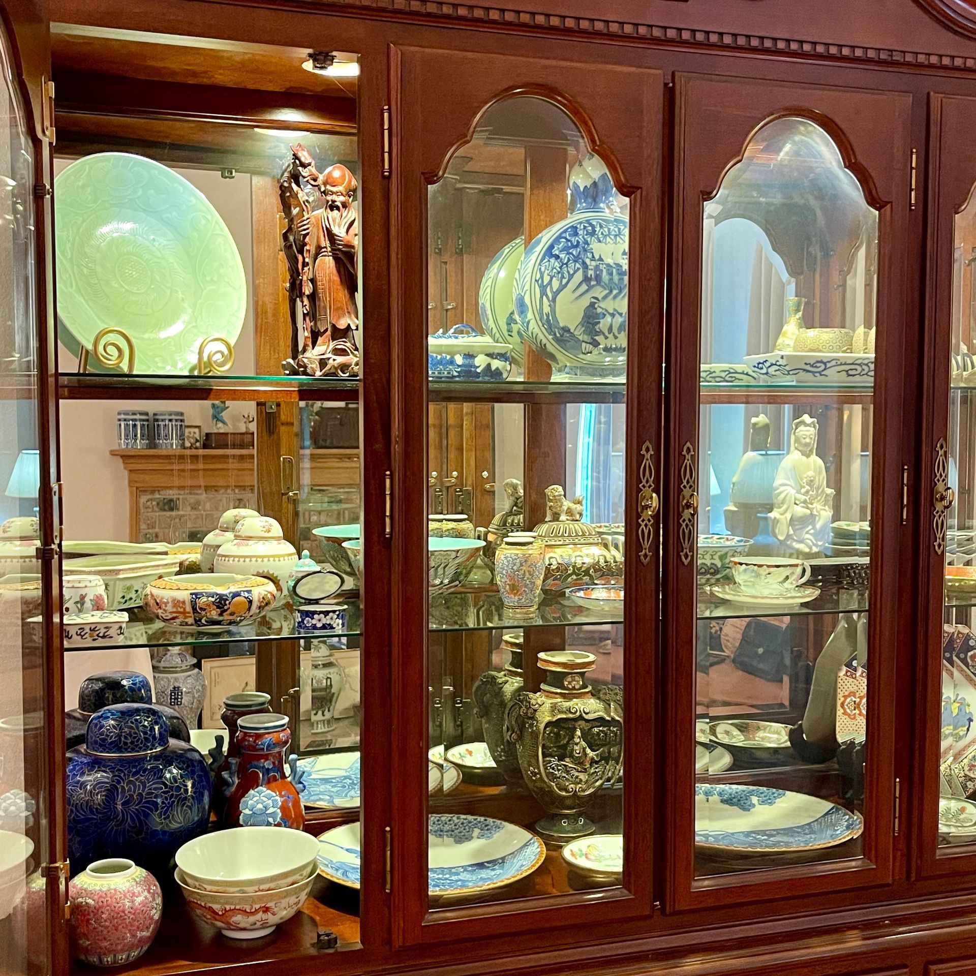 Wooden cabinet displaying decorative dishes, vases, and sculptures behind glass doors.