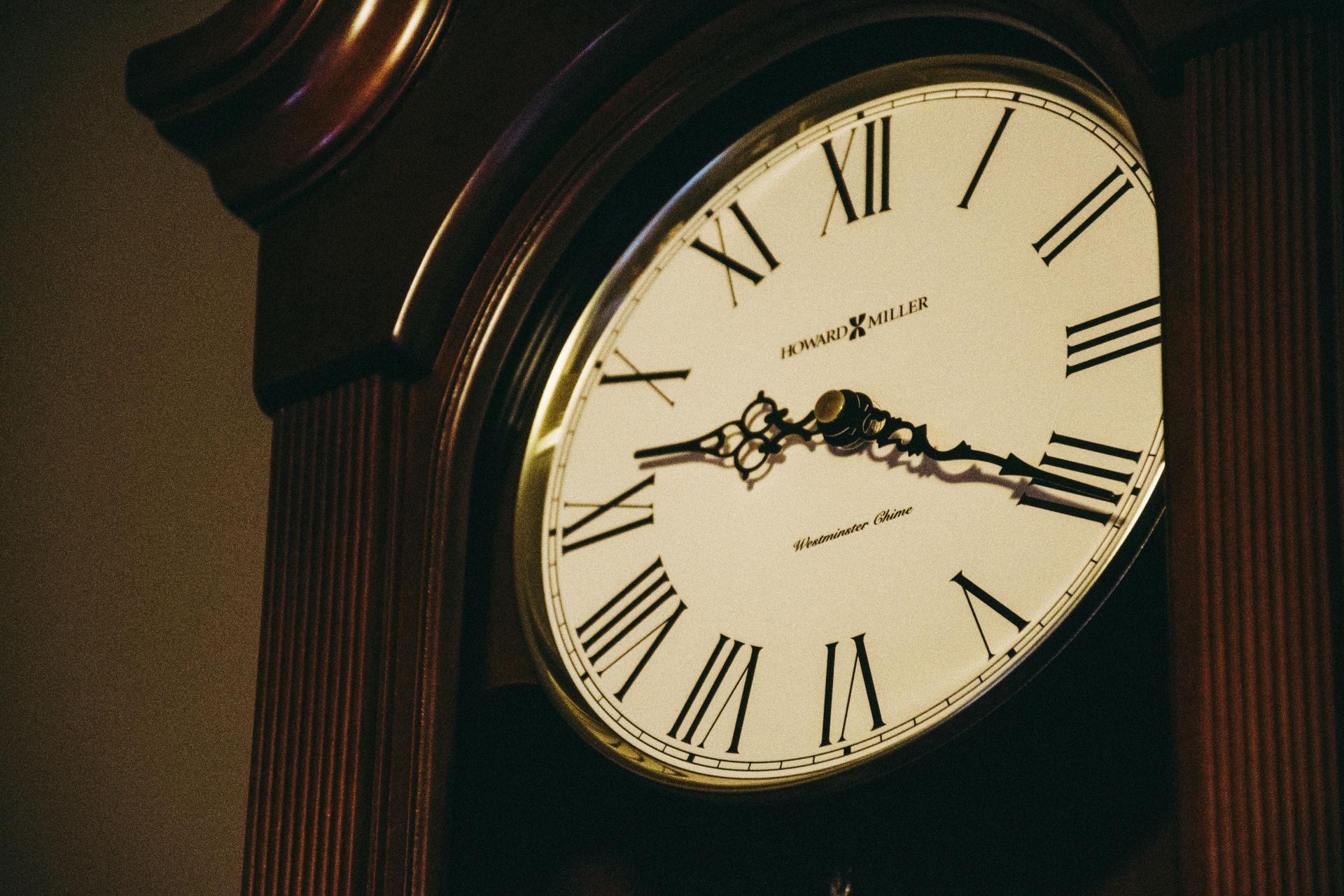 Close-up of a grandfather clock face, Roman numerals, ornate hands, and dark wooden frame.