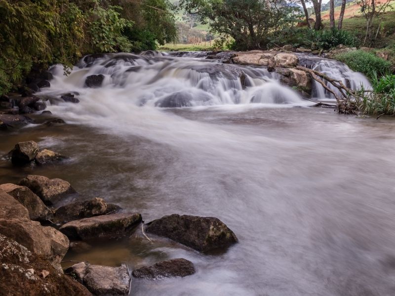 Cachoeira rochosa fluindo sobre pedras em uma paisagem arborizada.