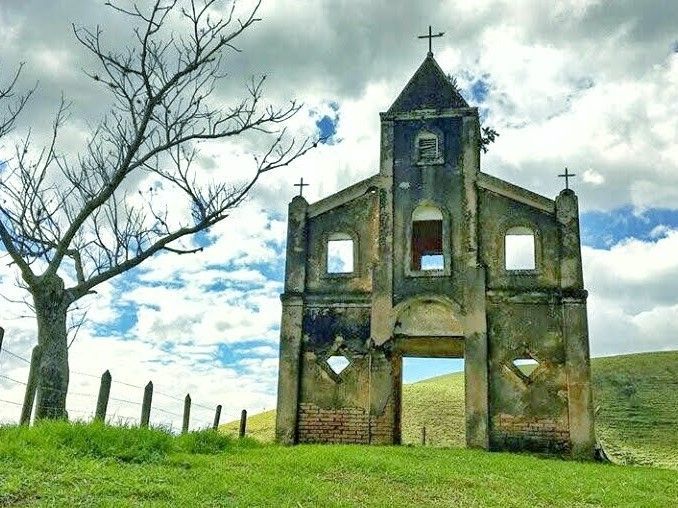Igreja de pedra em ruínas numa colina gramada sob um céu nublado.