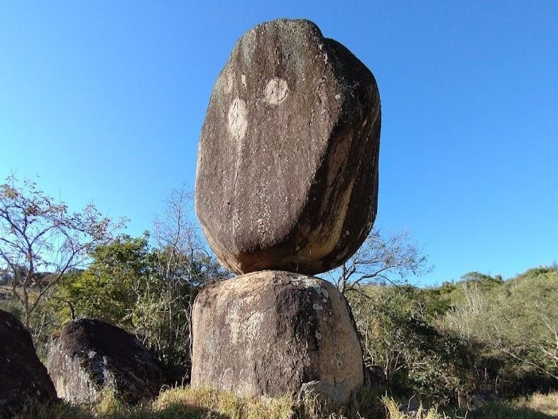 Duas rochas empilhadas, em equilíbrio como uma escultura, sob um céu azul límpido em uma paisagem rochosa.