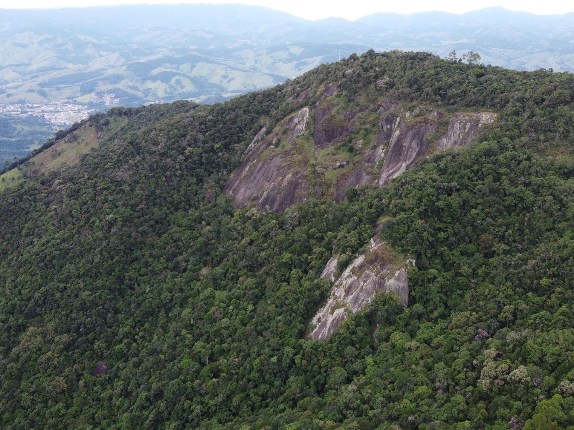 Cordilheira coberta de floresta com encostas rochosas expostas, com vista para um vale envolto em névoa.