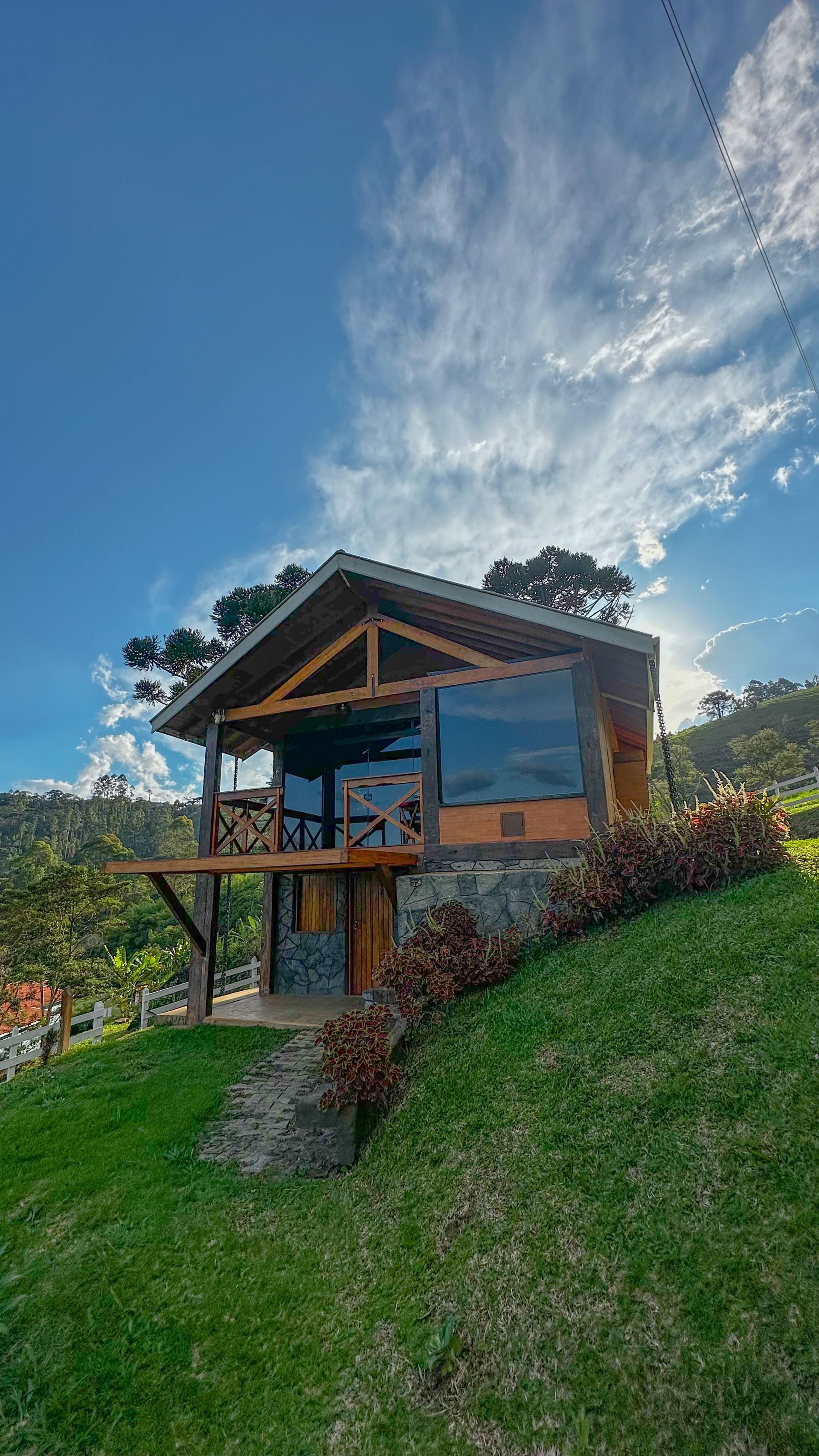 Cabana moderna em uma encosta gramada sob um céu azul com nuvens dramáticas.