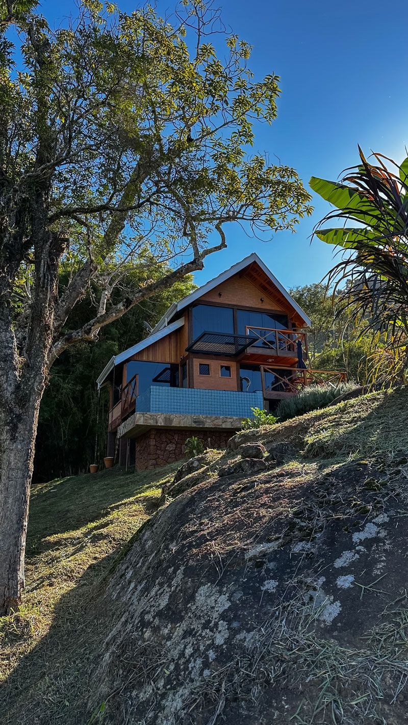 Cabana de madeira em uma encosta rochosa com árvores e céu azul ao fundo.